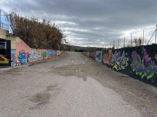 Section pavée de la piste cyclable entre des murs avec des graffitis. Entrée latérale sur la gauche, sous la voie ferrée